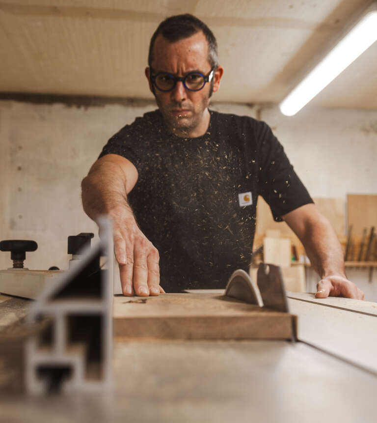 Sami Dubosc Artisan à l'œuvre dans l'atelier de la Manufacture Dubosc et Fils, travaillant sur des créations en bois massif. Fabrication artisanale et savoir-faire traditionnel pour des produits uniques et durables. Découvrez nos créations personnalisées sur notre boutique en ligne.