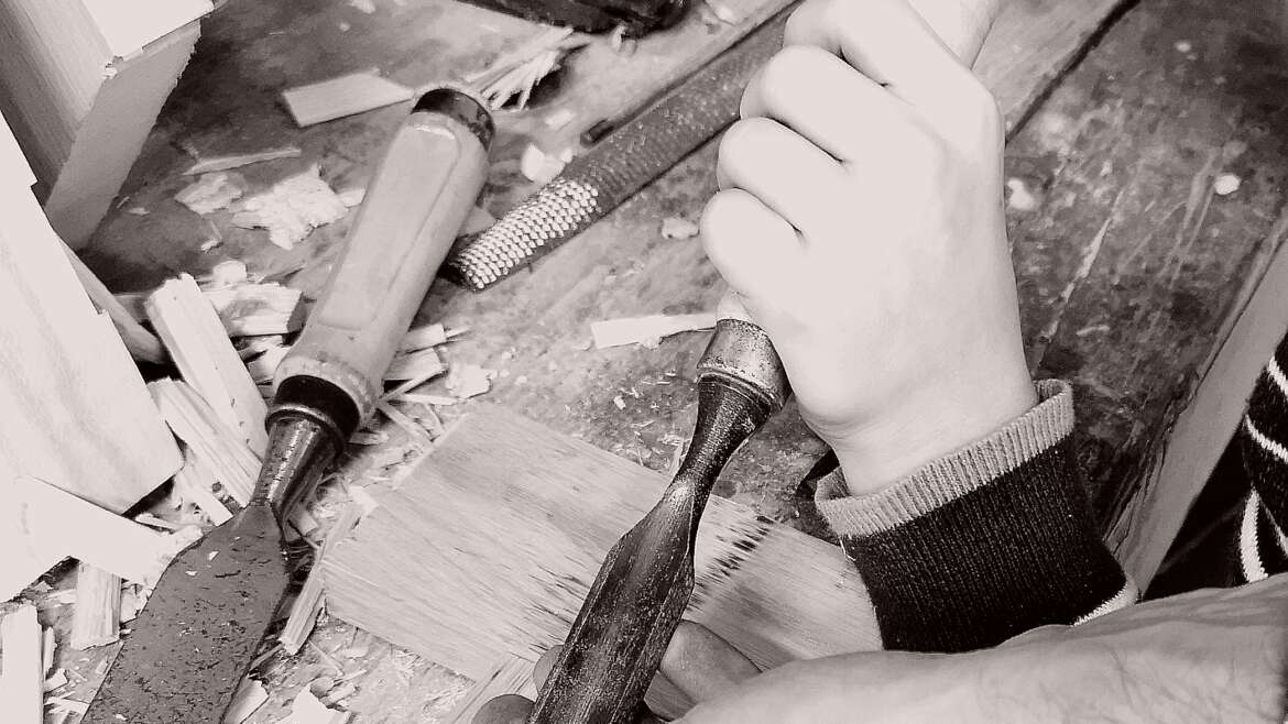 Initiation à l'ébénisterie chez Manufacture Dubosc et Fils, montrant un adulte guidant la main d'un enfant pour apprendre la sculpture sur bois. Cette image illustre la transmission du savoir-faire artisanal, l'importance du travail manuel et les valeurs de durabilité et d'artisanat familial portées par Manufacture Dubosc et Fils.