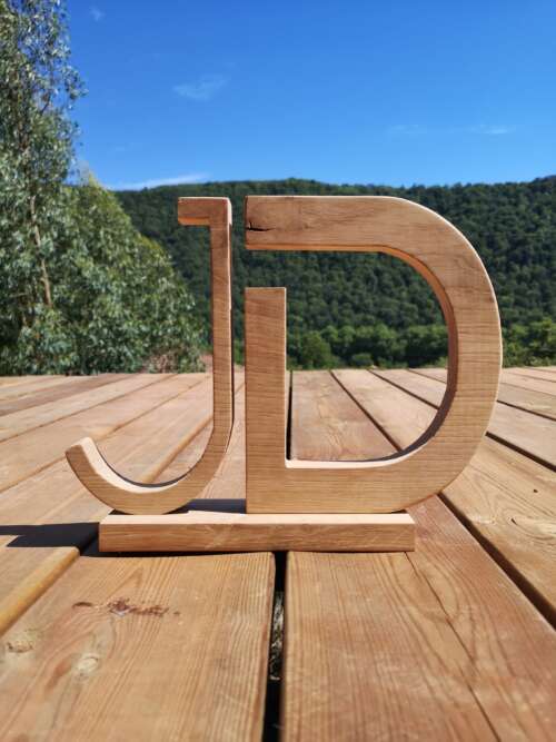 Lettrage 3D en bois massif sur un plancher derrière une colline verdoyante avec un beau ciel bleu