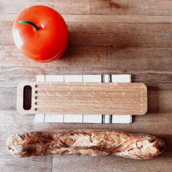 Planche à découper en chêne massif accompagnée d'une baguette de pain croustillante et d'une pomme pour une scène de cuisine chaleureuse et accueillante.