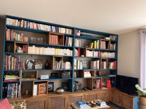 Bibliothèque remplie de livres avec des boites en chêne et des étagères peintes en bleu lagon.