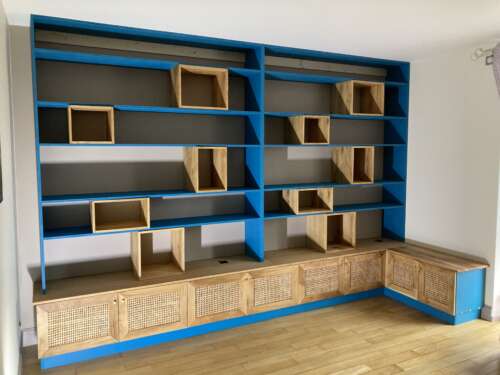 Bibliothèque sur mesure en bois massif de Manufacture Dubosc et Fils, avec des étagères peintes en bleu et des modules de rangement en bois naturel. Cette bibliothèque personnalisée met en valeur un design contemporain et une fabrication artisanale durable, idéale pour optimiser le rangement tout en ajoutant une touche esthétique à votre intérieur.