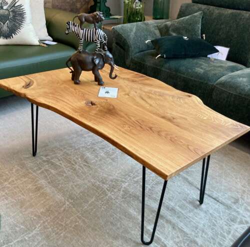 Table basse en chêne massif avec bord naturel conçue par Manufacture Dubosc et Fils, présentée dans un salon avec des figurines décoratives. Ce meuble artisanal au design organique est idéal pour apporter une touche authentique et rustique à votre intérieur. Découvrez nos tables basses en bois massif, fabriquées de manière durable et avec soin.