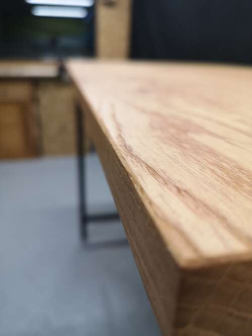 Gros plan sur le plateau en chêne massif d'une table de bistrot fabriquée par Manufacture Dubosc et Fils. Ce détail met en valeur la texture naturelle du bois et la qualité artisanale du travail, illustrant le soin apporté à chaque pièce de mobilier en bois massif que nous proposons. Idéale pour un espace moderne et chaleureux.