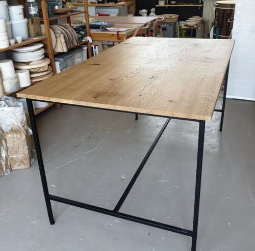 Table haute de style bistrot avec plateau en chêne massif et pieds en métal noir, réalisée sur mesure par Manufacture Dubosc et Fils. Idéale pour un atelier de céramiste, cette table en bois massif et acier apporte une touche industrielle tout en offrant robustesse et qualité artisanale. Mobilier durable conçu pour des espaces créatifs.