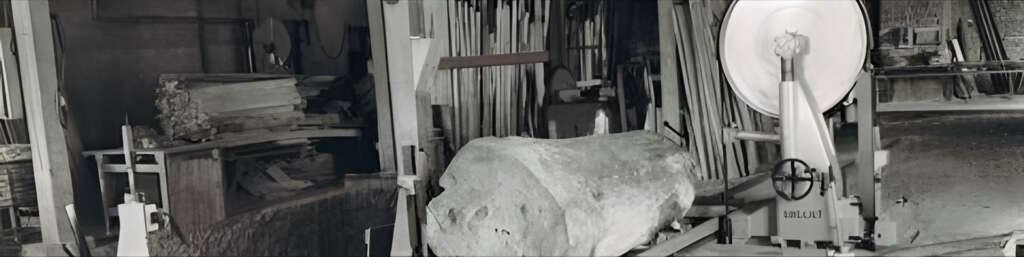 Atelier de sciage de bois de la scierie utilisée par Dubosc et Fils, en 1946, 4eme génerations de Dubosc dans le travail du bois, mettant en avant une scie de tête et des troncs de bois massif. Cette image illustre le savoir-faire traditionnel du travail du bois, essentiel pour la création de meubles artisanaux en bois durable. Manufacture Dubosc et Fils travaille en partenariat avec des scieries locales pour sélectionner les meilleurs matériaux, garantissant la qualité et la durabilité de chaque pièce fabriquée.