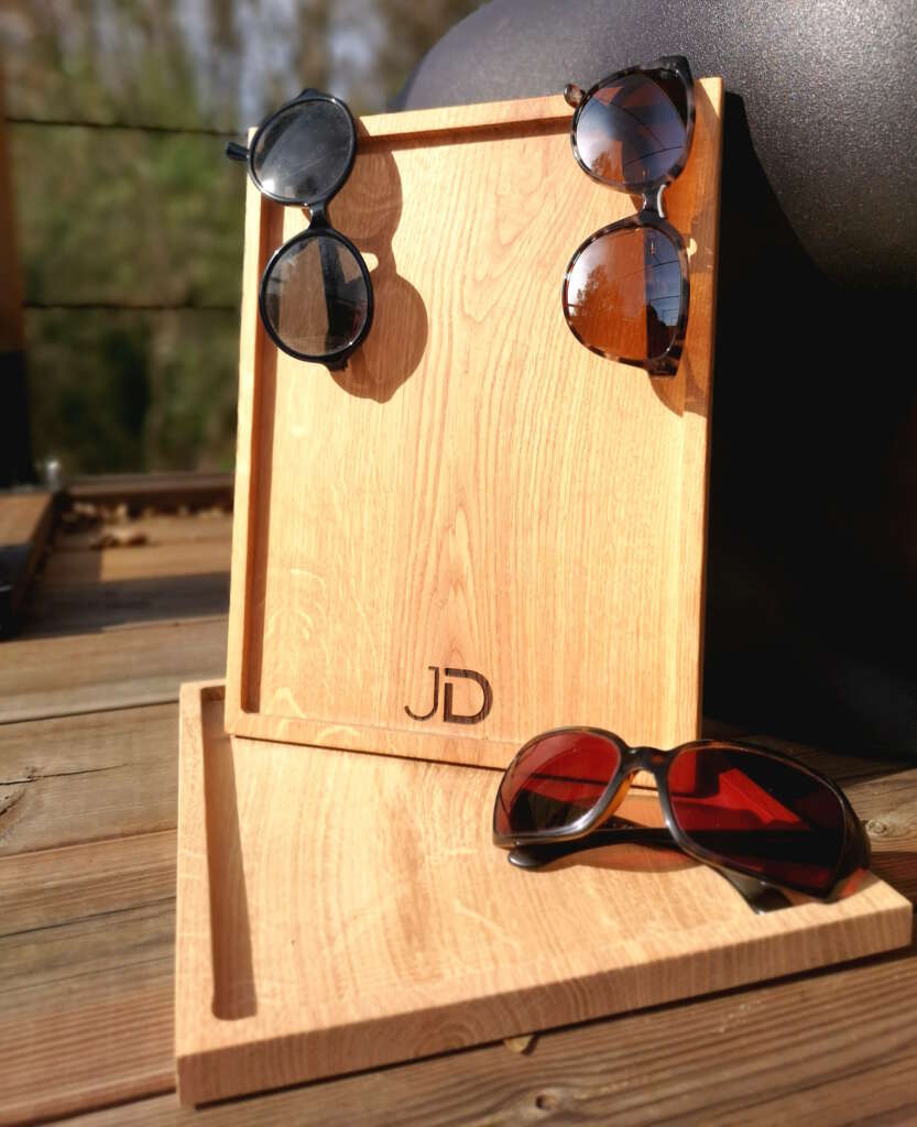 Plateaux en chêne massif personnalisés avec le logo JD, Jimmy Dubois Opticien conçus par Manufacture Dubosc et Fils, utilisés pour exposer des lunettes de soleil. Ces présentoirs artisanaux sont idéaux pour les boutiques cherchant à présenter leurs produits avec élégance. Les créations sur mesure de Manufacture Dubosc et Fils allient qualité, fonctionnalité et un design raffiné pour mettre en valeur les articles de manière unique.