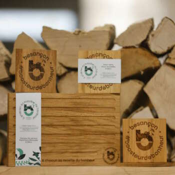 Photo de présentation de planches à découper en bois massif réalisées par Manufacture Dubosc et Fils, avec des gravures personnalisées "Besançon #boosteurdebonheur". Ces planches de qualité artisanale sont parfaites pour la cuisine et le service, conçues de manière durable à partir de bois local. Découvrez ces produits et bien d'autres créations sur notre boutique en ligne.