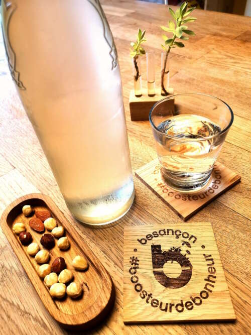 Plateau en bois massif de Manufacture Dubosc et Fils, contenant des noisettes et amandes, accompagné d'un sous-verre personnalisé "Besançon #boosteurdebonheur" et d'un support en bois pour plantes décoratives. Accessoires artisanaux fabriqués à partir de bois de haute qualité, parfaits pour créer une ambiance chaleureuse et naturelle dans votre intérieur. Découvrez notre gamme complète d'accessoires en bois durable sur notre boutique en ligne.