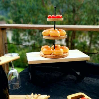 Présentoir à 3 niveaux en bois massif garni de pains et fruits lors d’un buffet élégant en extérieur.