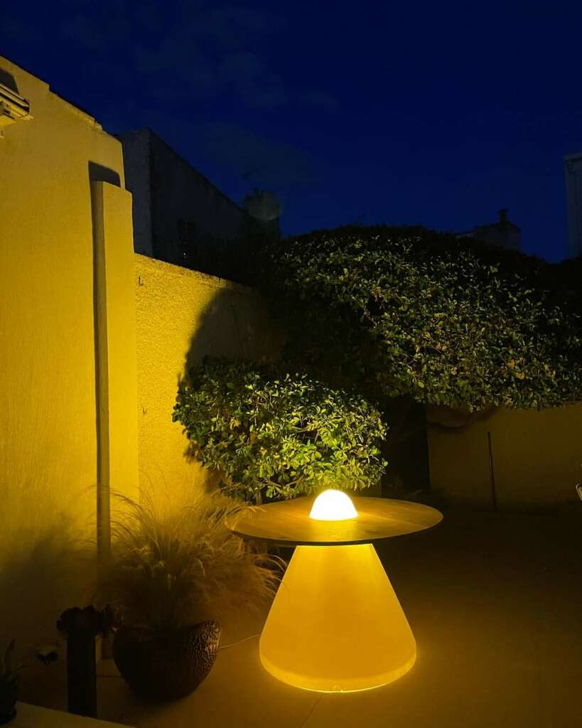 Table îlot lumineux en bois massif éclairée, installée dans un jardin pendant la nuit. Cette table artisanale au design unique, fabriquée avec des matériaux durables et éco-responsables, apporte une lumière douce et une ambiance chaleureuse aux soirées en extérieur. Idéale pour créer un espace accueillant et moderne, elle est le fruit d'un savoir-faire artisanal de qualité supérieure, proposé par notre boutique en ligne spécialisée en mobilier personnalisé.