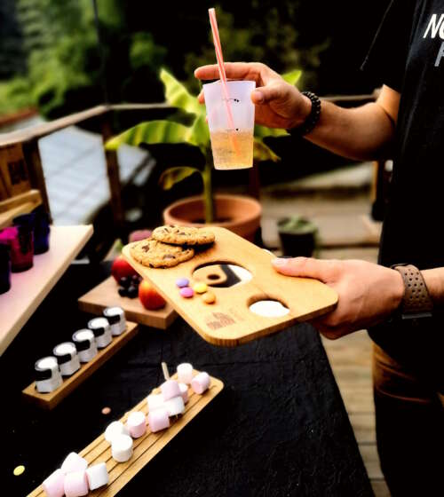 Planche apéritif en bois massif éco-responsable, faite main, avec un design fonctionnel permettant de tenir un eco-cup réutilisable et des snacks. Accessoire en bois durable, fabriqué artisanalement à partir de matériaux recyclés, incarnant le savoir-faire local et une approche zéro déchet. Idéal pour des événements, avec une éthique de fabrication et un design sur-mesure