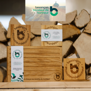 Ensemble de produits en bois personnalisés de la Manufacture Dubosc et Fils, comprenant des sous-verres et une planche de service en chêne massif, gravés avec les logos "Besançon, Boosteur de Bonheur" et "À chacun sa recette du bonheur" . Ces créations en bois massif sont conçues dans un esprit de durabilité, fabriquées à la main en France avec des matériaux éco-responsables. Idéales pour la décoration et l'usage quotidien, elles allient artisanat et élégance. Parfait pour les amoureux du bois et du design écologique.