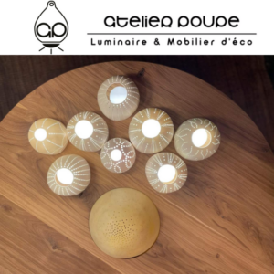 Collection de luminaires artisanaux posés sur une table en bois massif, réalisée par Atelier Poupe et Manufacture Dubosc et Fils. Les lampes présentent des motifs détaillés élégants et diffusent une lumière douce et chaleureuse, idéale pour créer une ambiance cocooning et naturelle. Le plateau de table en bois massif, fabriqué sur mesure par Manufacture Dubosc et Fils, allie design écologique et artisanat local. Ensemble parfait pour les intérieurs qui valorisent durabilité et esthétique artisanale, disponible sur le site Manufacture Dubosc et Fils.