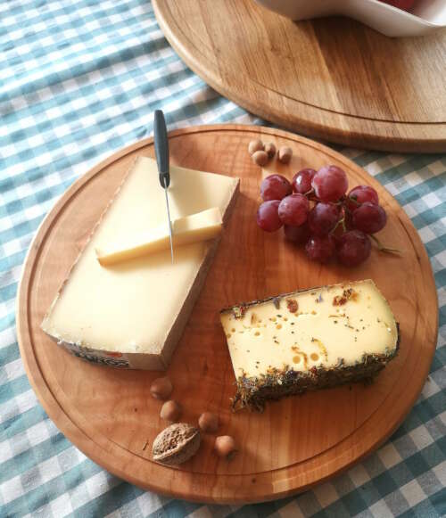 Plateau tournant en bois massif de 35 cm de Manufacture Dubosc et Fils, avec un morceau de comté, une tranche de tomme aux fleurs, des raisins, et des noisettes. Ce plateau artisanal est idéal pour les présentations de fromage et charcuterie, offrant une touche élégante et conviviale aux repas.