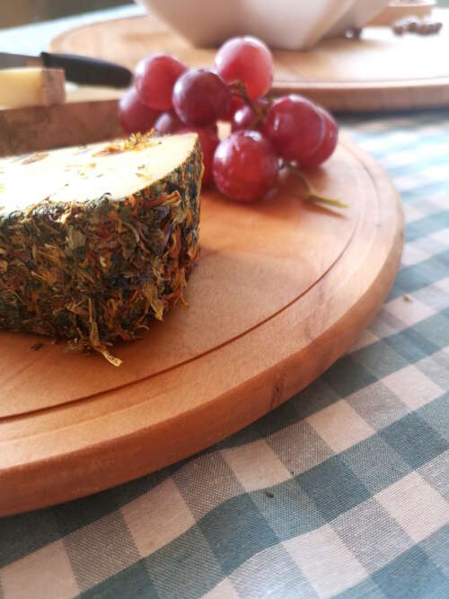 Vue rapprochée d'un plateau tournant en bois massif de 35 cm de Manufacture Dubosc et Fils, présentant un morceau de fromage affiné aux herbes et des grappes de raisin. Ce plateau en bois naturel est parfait pour sublimer les présentations de fromage et de charcuterie lors de repas conviviaux et élégants.