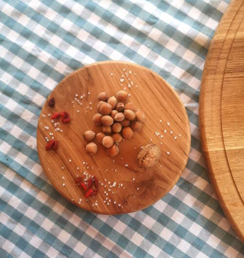 Petit plateau tournant en chêne massif de Manufacture Dubosc et Fils, décoré de noisettes, d'une noix, de baies de goji et de gros sel, sur une nappe à carreaux bleus et blancs. Ce plateau en bois naturel est idéal pour des présentations élégantes et conviviales, parfait pour sublimer vos apéritifs ou ingrédients.