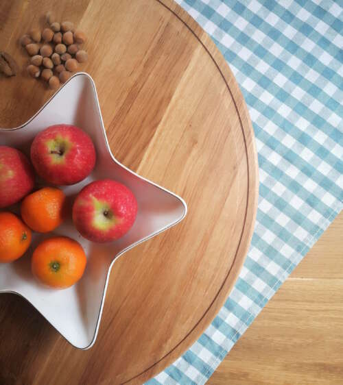 Plateau tournant en chêne massif de Manufacture Dubosc et Fils, agrémenté de pommes et de clémentines dans un plat en forme d'étoile. Ce plateau en bois, au design naturel et élégant, est parfait pour des présentations de table conviviales et chaleureuses.