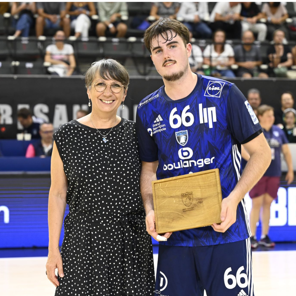 Remise de la récompense de l'homme du match lors d'un match du Grand Besançon Doubs Handball (GBDH), avec une planche en chêne massif gravée offerte par Manufacture Dubosc et Fils. Anne Vignot, maire de Besançon, félicite le joueur pour sa performance exceptionnelle. Cette création artisanale reflète l’engagement de notre entreprise pour célébrer les talents sportifs et promouvoir un artisanat local et durable.