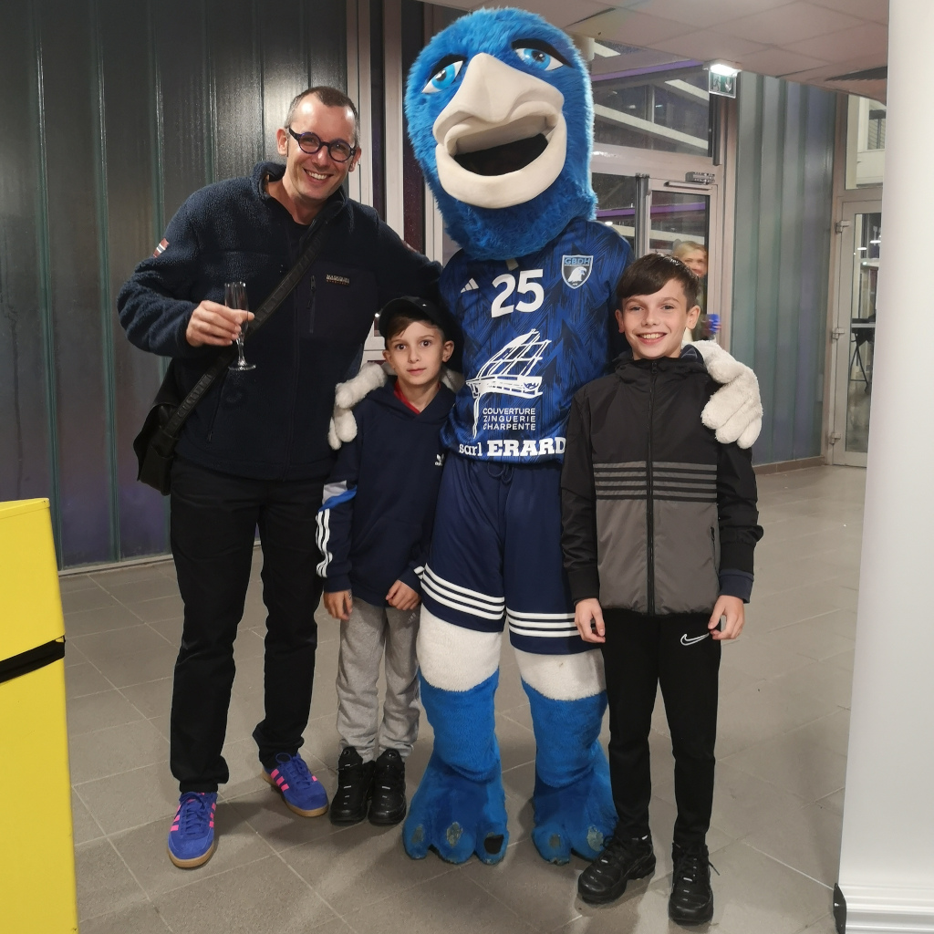 Rencontre conviviale avec la mascotte du Grand Besançon Doubs Handball (GBDH) : Sami Dubosc, fondateur de la Manufacture Dubosc et Fils, accompagné de ses enfants, partage un moment familial après un match. Une belle occasion de souligner l’engagement artisanal et local de la Manufacture à travers la création de plateaux en bois massif gravés pour récompenser l’homme du match.