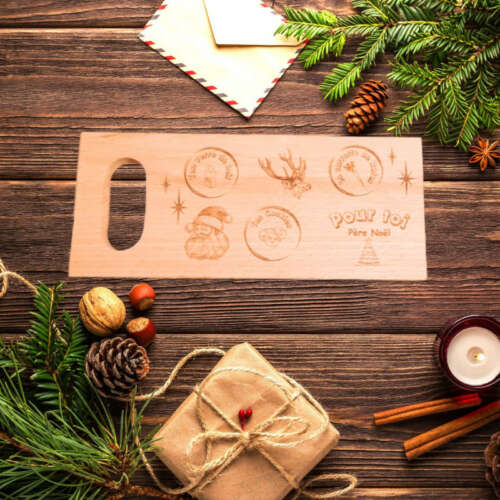 Planche de Noël en bois massif gravée par Manufacture Dubosc et Fils, entourée d'un décor festif de Noël avec des branches de sapin, des noix et des lettres au Père Noël. Cette planche artisanale est idéale pour apporter une touche chaleureuse et personnalisée aux fêtes de fin d'année. Un cadeau unique, parfait pour célébrer Noël avec authenticité et une touche d'artisanat.