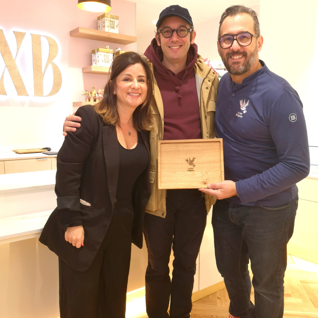 Une rencontre chaleureuse dans la boutique du maître chocolatier Xavier Brignon . Au centre, Sami Dubosc, artisan créateur de la Manufacture Dubosc et Fils , tient fièrement une élégant plateau de service en chêne massif personnalisée gravée du logo de Xavier Brignon. Cette collaboration célèbre l'artisanat local et l'excellence du savoir-faire français, combinant bois de qualité et chocolats artisanaux. Un partenariat unique mettant en avant des cadeaux sur mesure pour entreprises ou particuliers, parfaits pour les événements et fêtes de fin d'année.