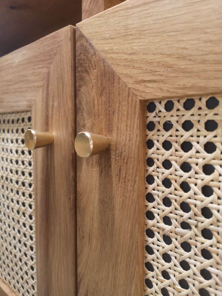 Détail des finitions d'un meuble sur mesure en chêne massif avec cannage naturel et poignée en laiton.