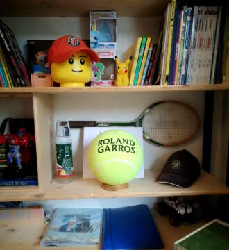 Support de balle de tennis en chêne massif mettant en valeur une balle souvenir dans une bibliothèque personnelle.