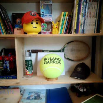 Support de balle de tennis en chêne massif mettant en valeur une balle souvenir dans une bibliothèque personnelle.